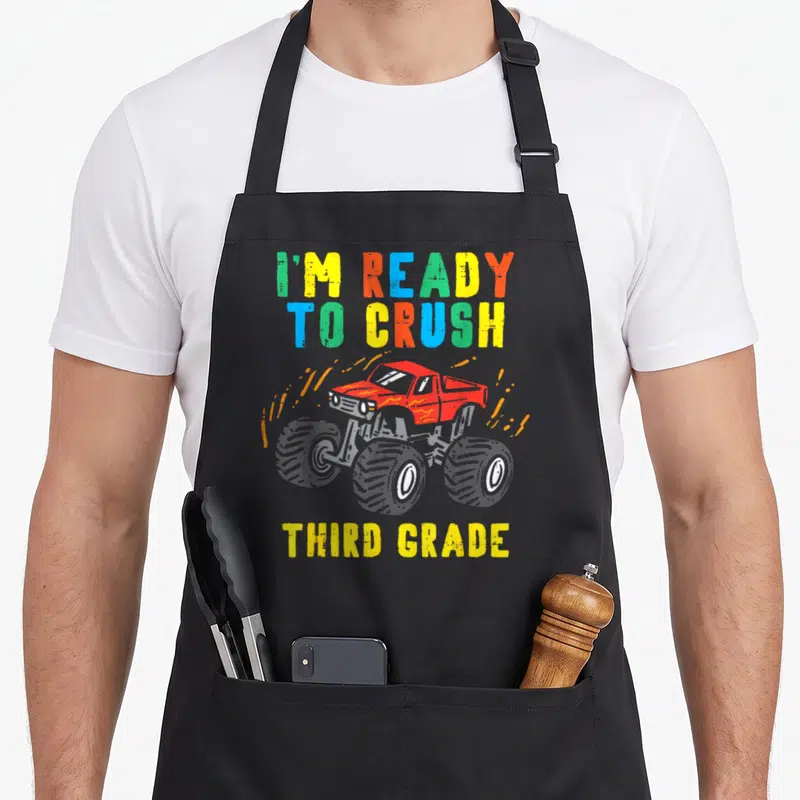 Crush 3rd truck apron - Red monster truck with colorful text I'm ready to crush third grade — shown on a black cotton canvas apron against a white background