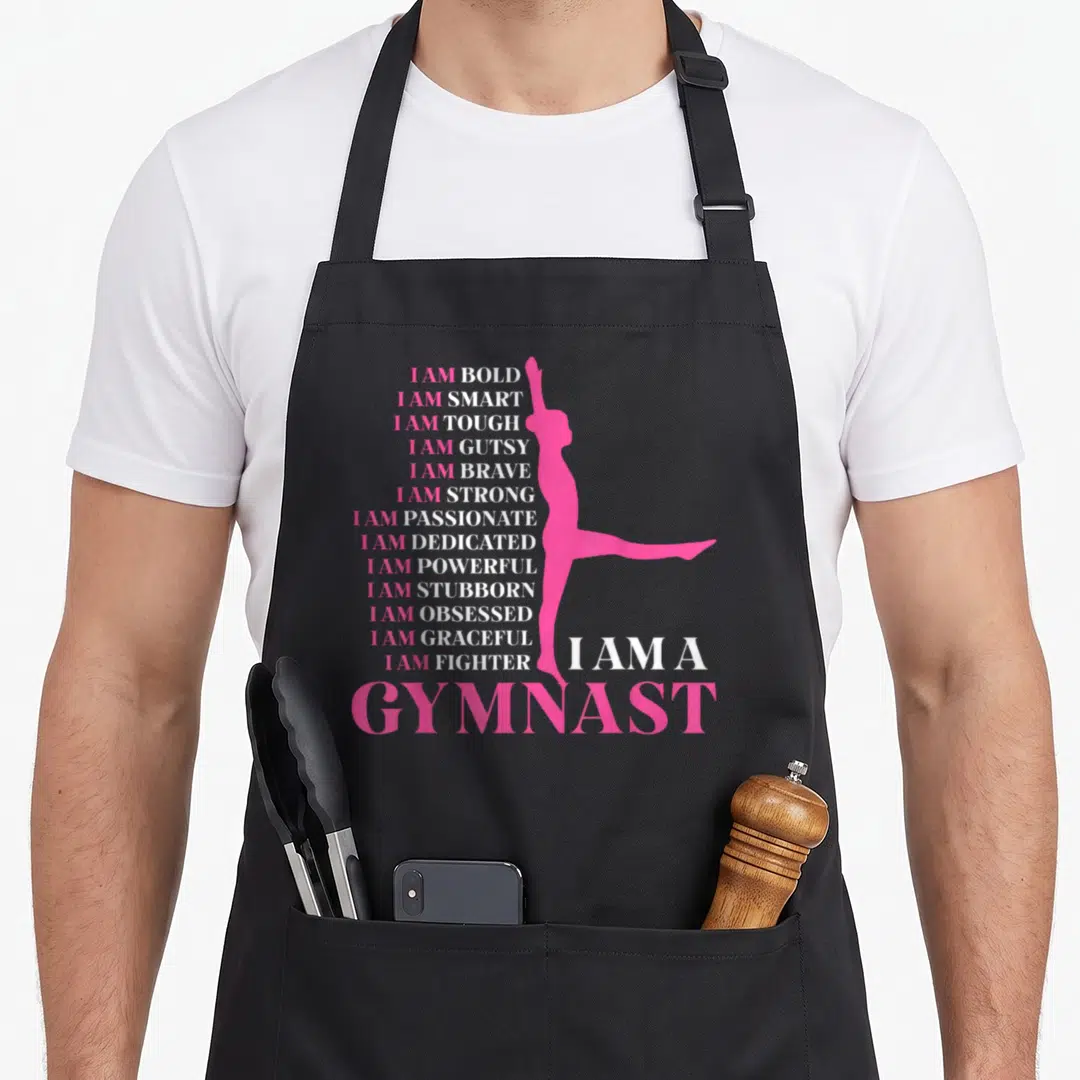 Sport gymnastics apron - Pink gymnast silhouette beside stacked white and pink I AM text ending with I AM A GYMNAST — shown on a black cotton canvas apron against a white background