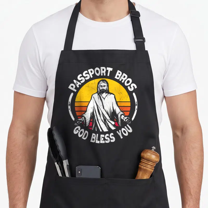 Passport meme apron - Jesus figure with Passport Bros text over striped retro sun in distressed white yellow orange red — shown on a black cotton canvas apron against a white background
