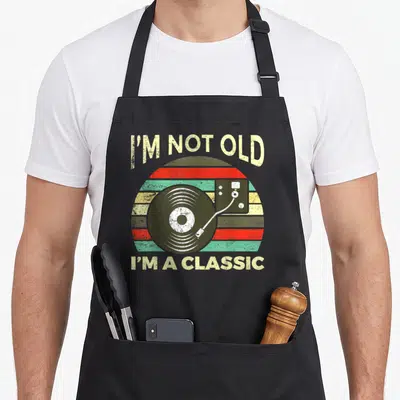Funny music vinyl apron - Record player graphic with striped sun background and text I'm not old I'm classic — shown on a black cotton canvas apron against a white background