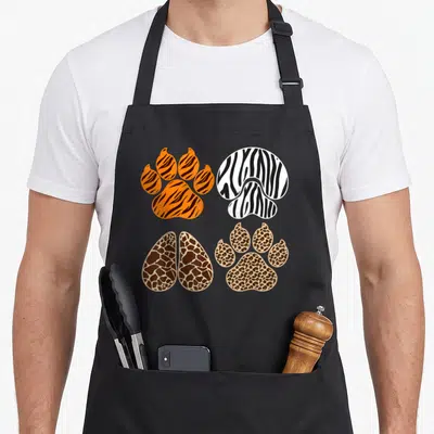 Toddler animal print apron - Four paw prints in orange, black, white, brown, beige with tiger, zebra, giraffe — shown on a black cotton canvas apron against a white background
