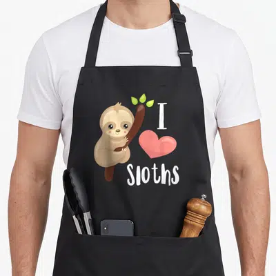 Funny animal sloth apron - Cartoon brown sloth clinging to branch next to pink heart and white I love Sloths text — shown on a black cotton canvas apron against a white background