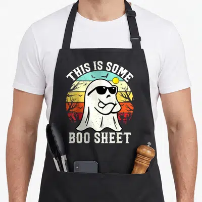 Sheet ghost halloween apron - Cartoon ghost in sunglasses over retro sunset with text THIS IS SOME BOO SHEET — shown on a black cotton canvas apron against a white background