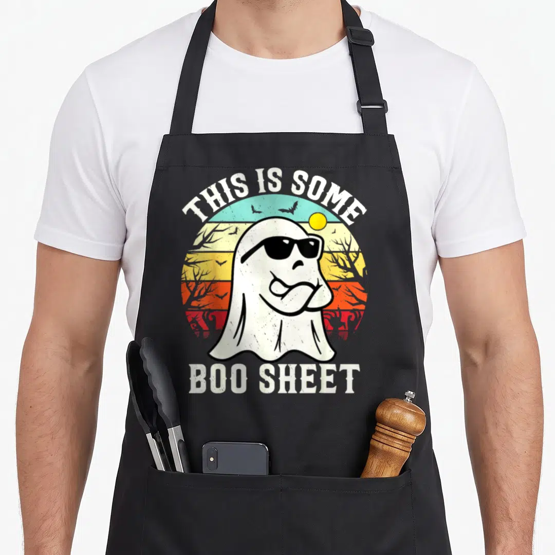 Sheet ghost halloween apron - Cartoon ghost in sunglasses over retro sunset with text THIS IS SOME BOO SHEET — shown on a black cotton canvas apron against a white background
