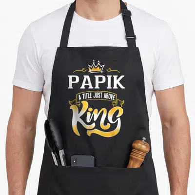 Papik king apron - Crown and PAPIK A Title Just Above King text in white and yellow typography — shown on a black cotton canvas apron against a white background