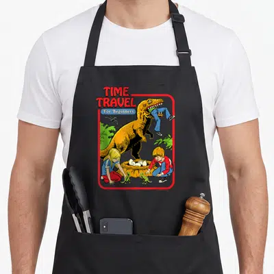 Steven dinosaur apron - T-Rex eating legs near crouching children and eggs under TIME TRAVEL For Beginners text — shown on a black cotton canvas apron against a white background