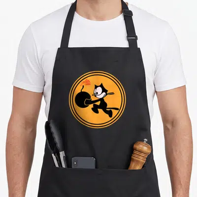 Ww2 cat apron - Cartoon black cat carrying bomb inside orange circle with black rings — shown on a black cotton canvas apron against a white background