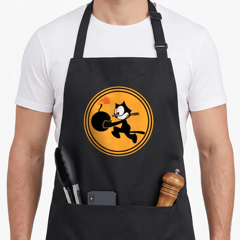 Ww2 cat apron - Cartoon black cat carrying bomb inside orange circle with black rings — shown on a black cotton canvas apron against a white background