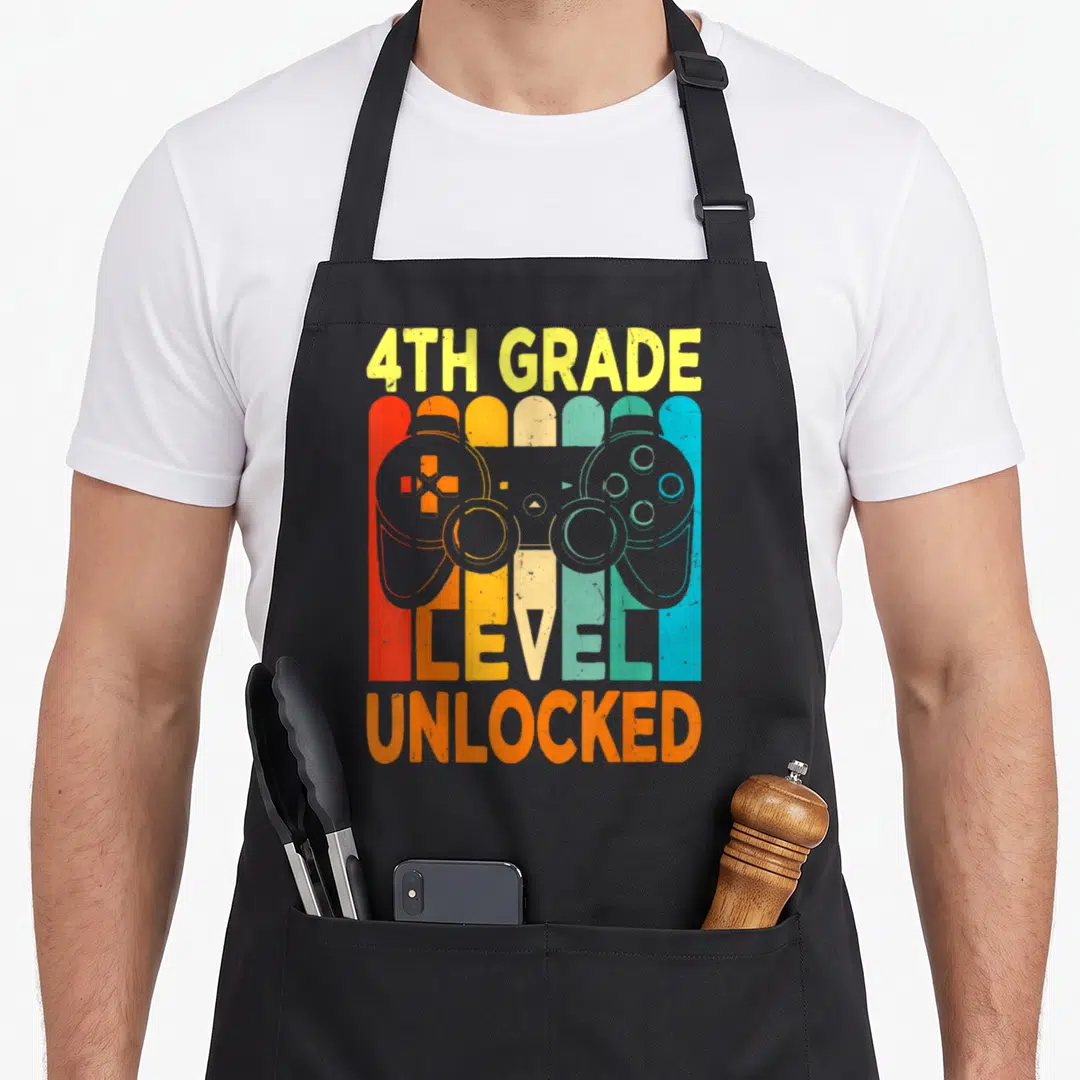Hello 4th video game apron - Grey game controller silhouette over five colorful vertical stripes with 4TH GRADE text — shown on a black cotton canvas apron against a white background