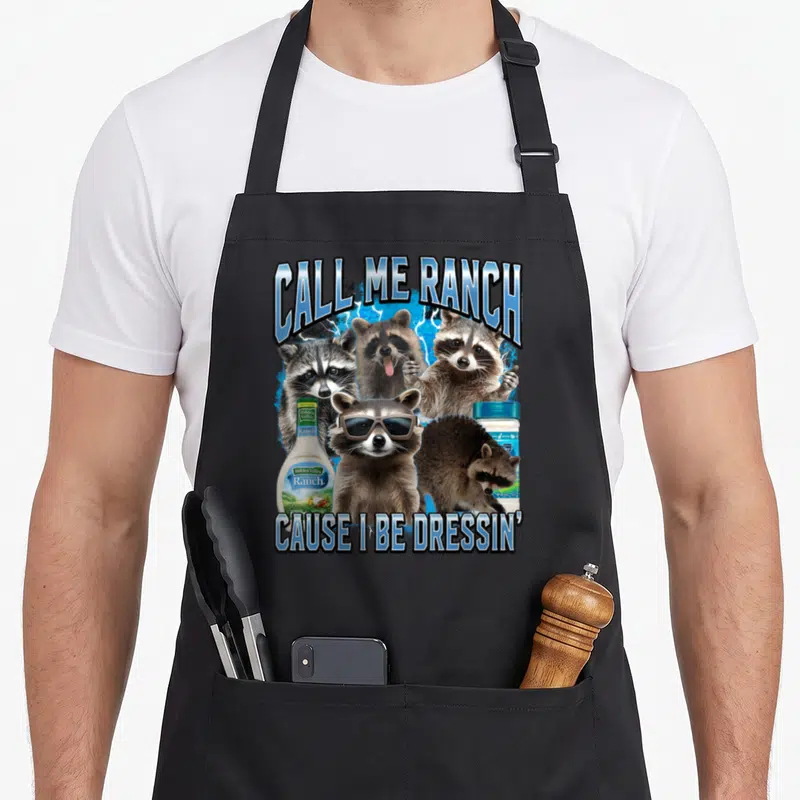 Ranch meme apron - Four raccoons and two ranch dressing bottles on blue lightning with text — shown on a black cotton canvas apron against a white background