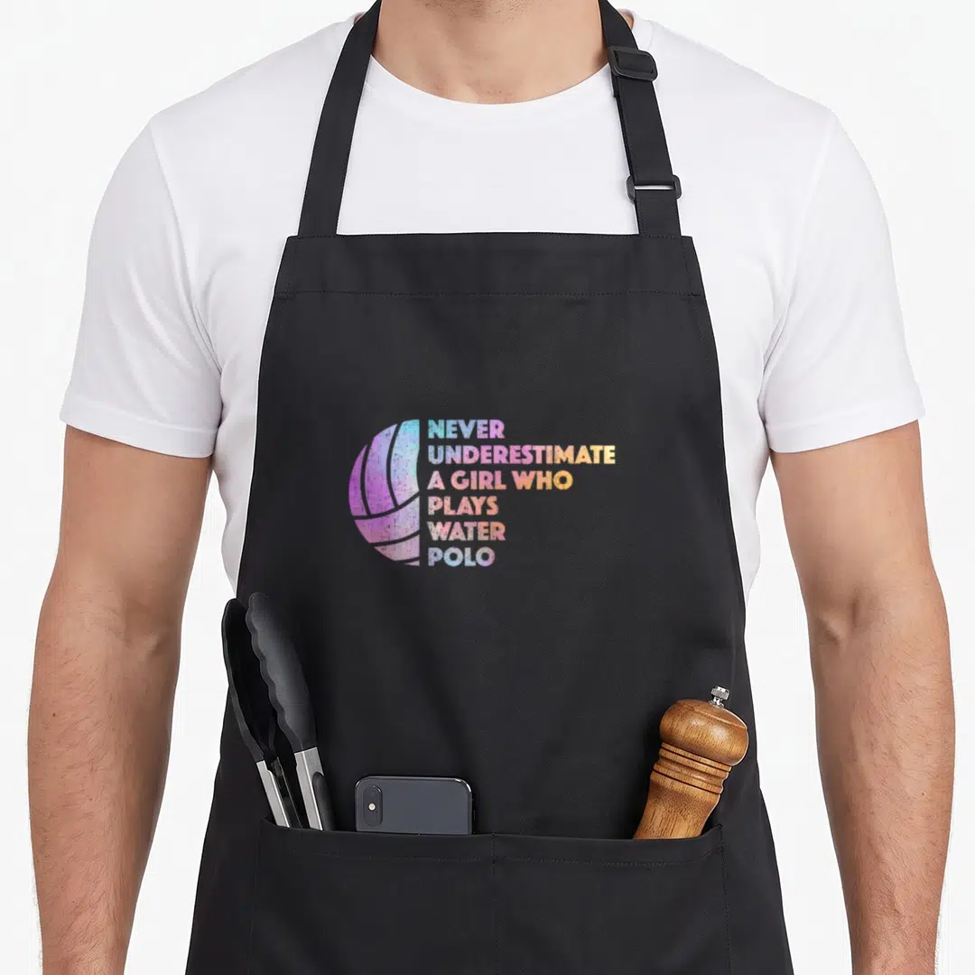 Athlete water polo apron - Colorful water polo ball next to stacked text reading never underestimate a girl who plays — shown on a black cotton canvas apron against a white background