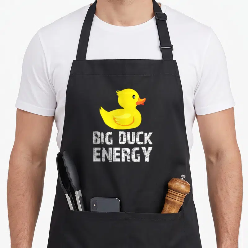 Energy duck apron - Yellow cartoon duck above white distressed BIG DUCK ENERGY text — shown on a black cotton canvas apron against a white background