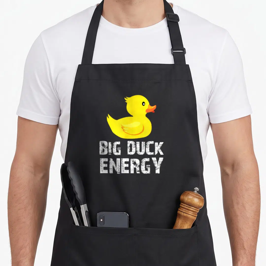 Energy duck apron - Yellow cartoon duck above white distressed BIG DUCK ENERGY text — shown on a black cotton canvas apron against a white background