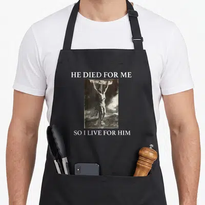 Our christian apron - White text HE DIED FOR ME above a black and white photo of Jesus on the cross — shown on a black cotton canvas apron against a white background