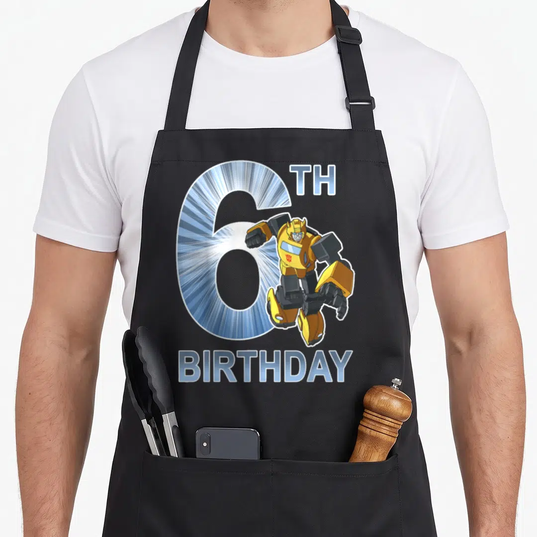 Bumblebee 6th birthday apron - Cartoon Bumblebee robot overlapping a large blue number 6 with TH BIRTHDAY text — shown on a black cotton canvas apron against a white background