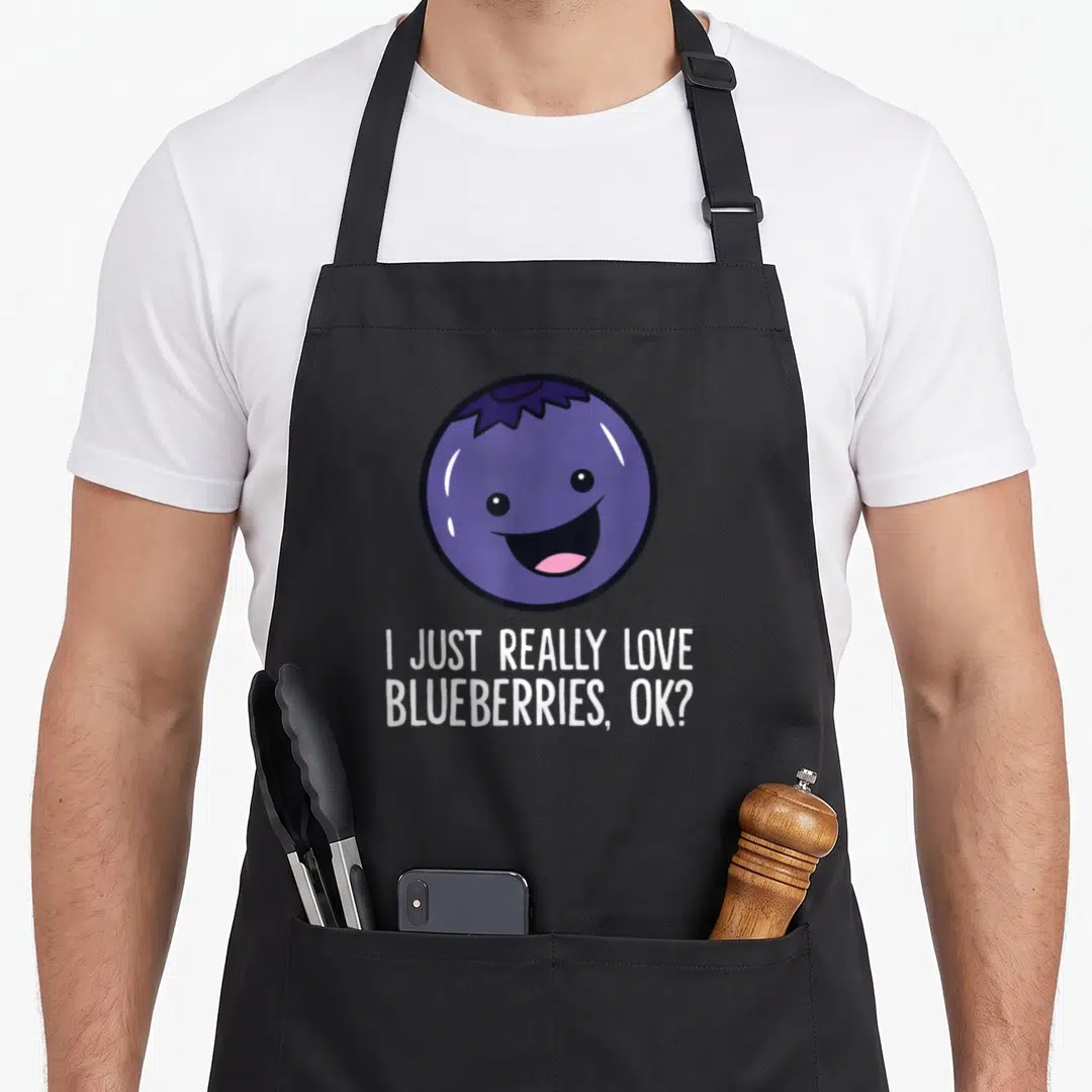 Blueberry kawaii apron - Smiling purple cartoon blueberry above white text reading I just really love blueberries ok — shown on a black cotton canvas apron against a white background