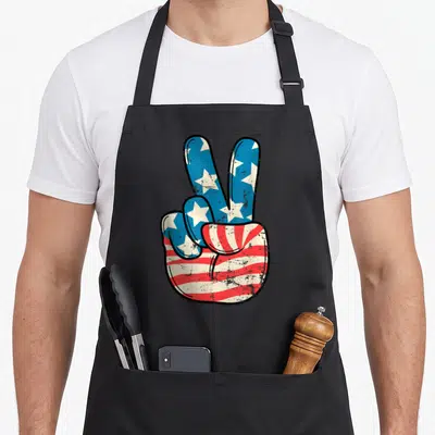 Hand 4th of july apron - Distressed hand peace sign filled with red white and blue stars and stripes pattern — shown on a black cotton canvas apron against a white background