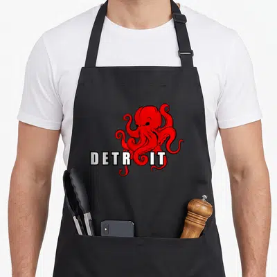 Octopus detroit apron - Red cartoon octopus overlapping white block letters spelling DETROIT with black outlines — shown on a black cotton canvas apron against a white background