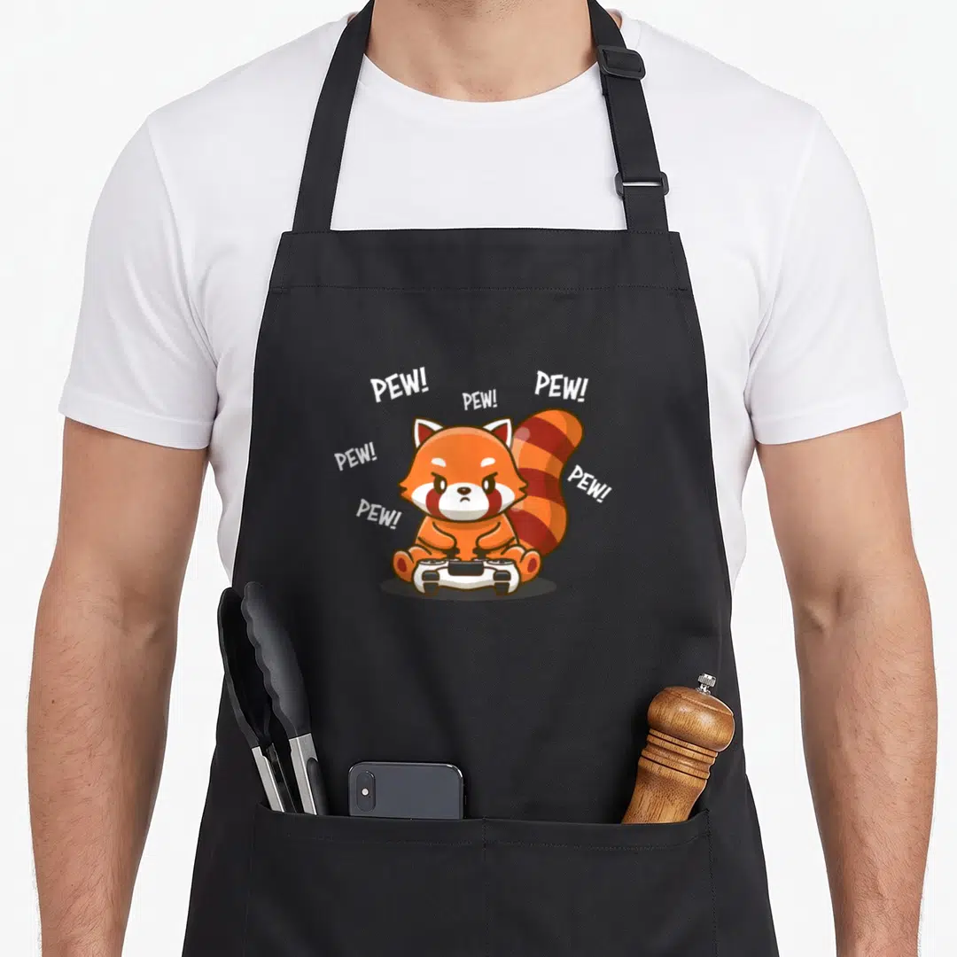 Video kawaii apron - Red panda holding controller with PEW text arch in orange, white, and black cartoon style — shown on a black cotton canvas apron against a white background