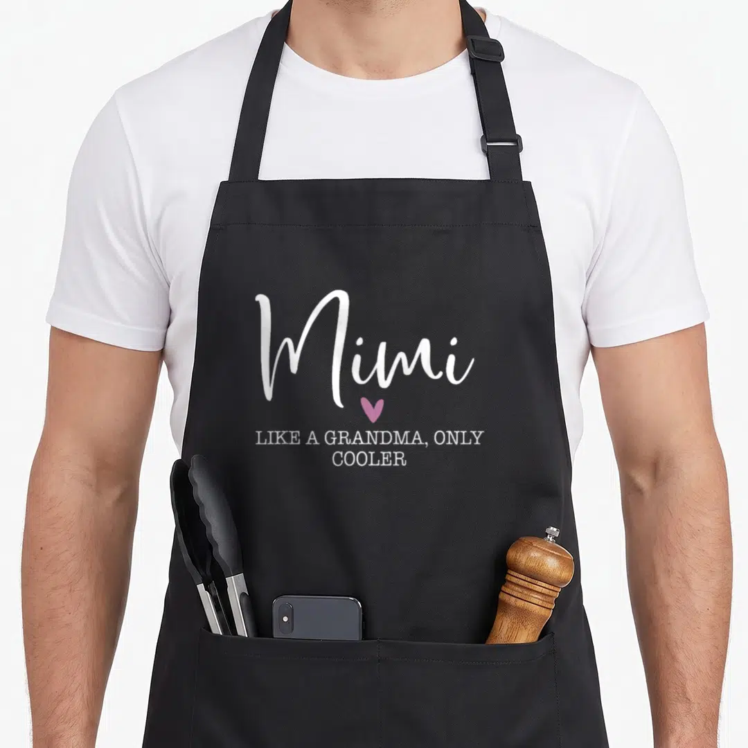 Mimi grandma mother's day aprons - White Mimi script text above a pink heart and Like A Grandma Only Cooler words — shown on a black cotton canvas apron against a white background