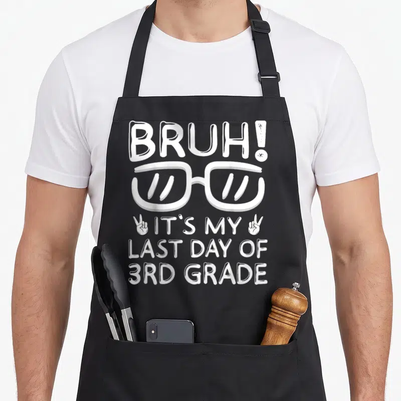 3rd bruh grade apron - White BRUH text, glasses, and peace sign hands printed on black bib — shown on a black cotton canvas apron against a white background
