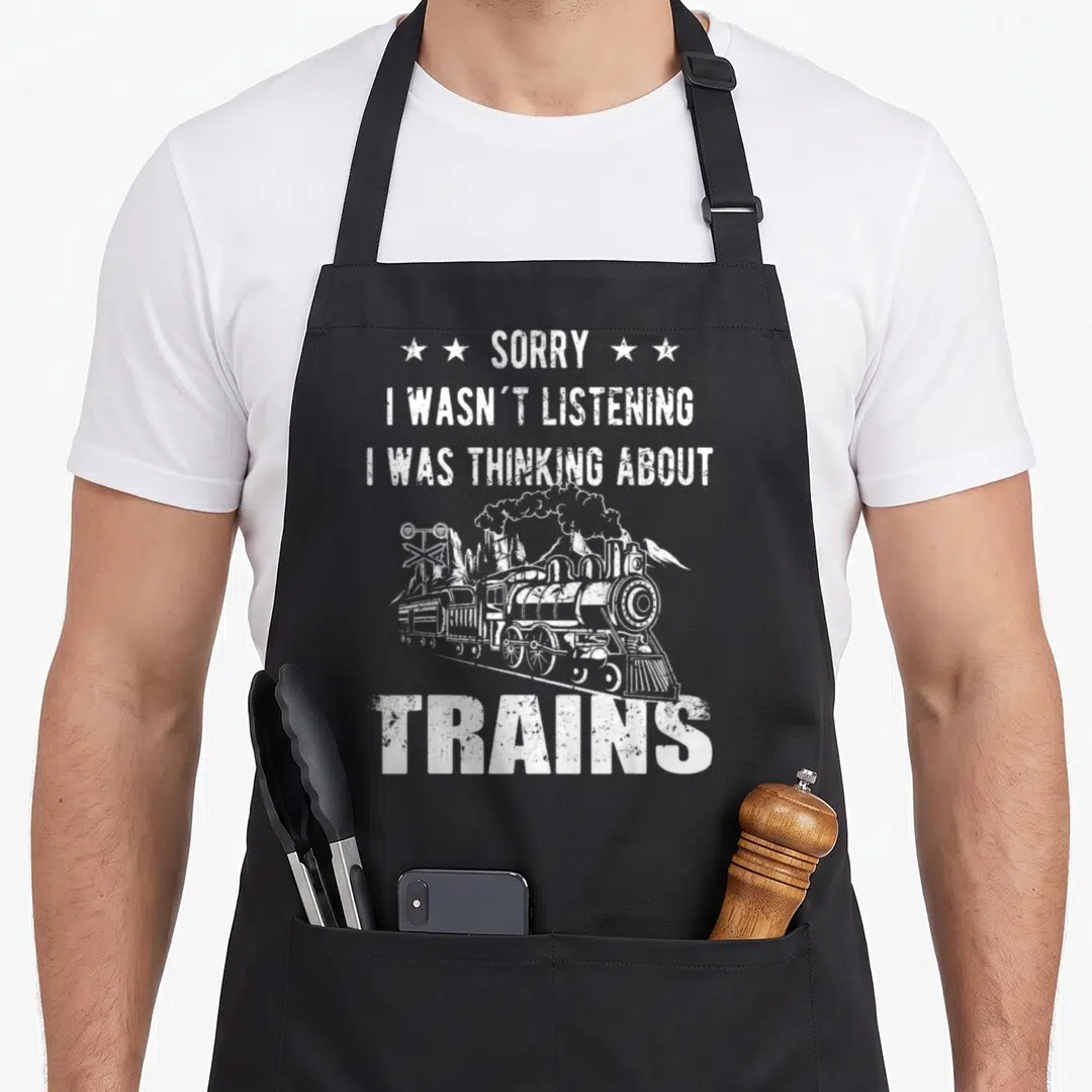 Sorry railroad train apron - White distressed text Sorry I Wasnt Listening I Was Thinking About Trains above steam — shown on a black cotton canvas apron against a white background