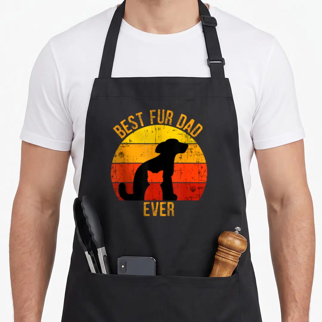 Fur dog funny cat aprons - Retro sunset with black dog silhouette containing a cat shape and BEST FUR DAD text — shown on a black cotton canvas apron against a white background