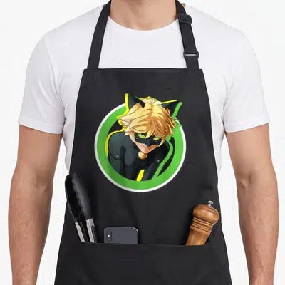 Miraculous cat apron - Cartoon character facing forward in green circle with white border, black suit, blonde hair — shown on a black cotton canvas apron against a white background