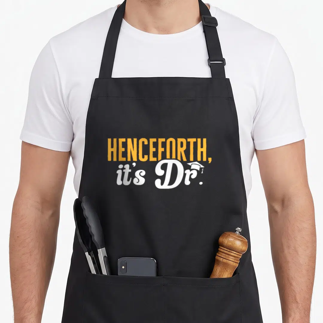 Phd dr apron - Orange and white text reading Henceforth It's Dr with a small graduation cap icon on the letter r — shown on a black cotton canvas apron against a white background