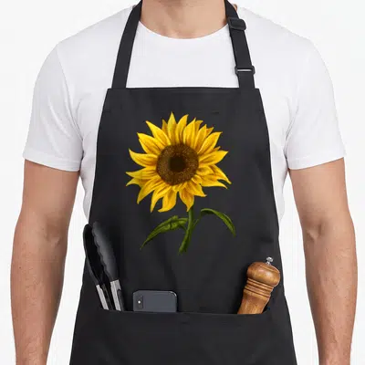 Sunshine floral apron - Realistic watercolor sunflower with yellow petals, brown center, and green stem and leaves — shown on a black cotton canvas apron against a white background