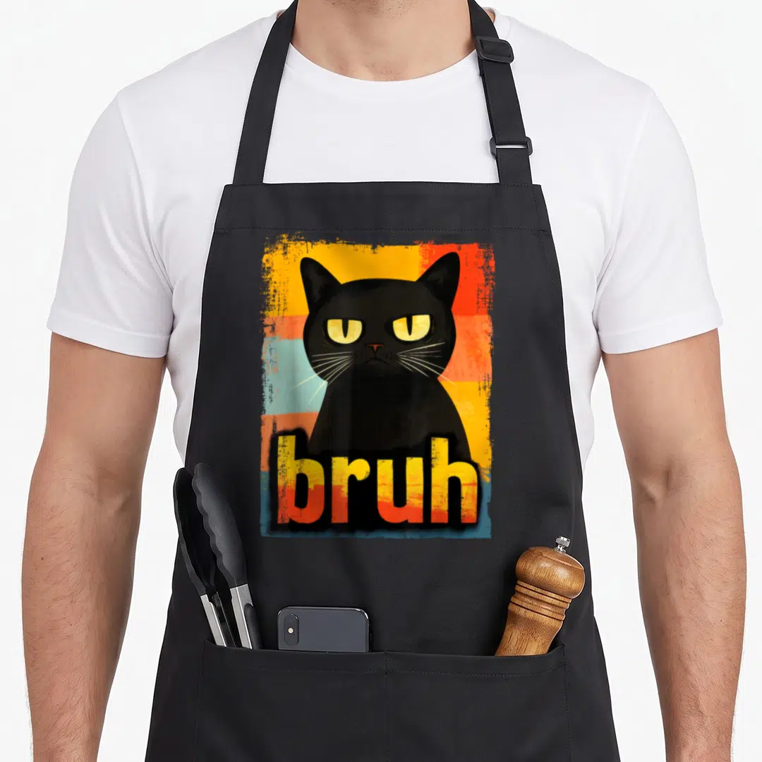 Bruh cat apron - Grumpy black cat illustration with bruh text on distressed multicolored stripes — shown on a black cotton canvas apron against a white background