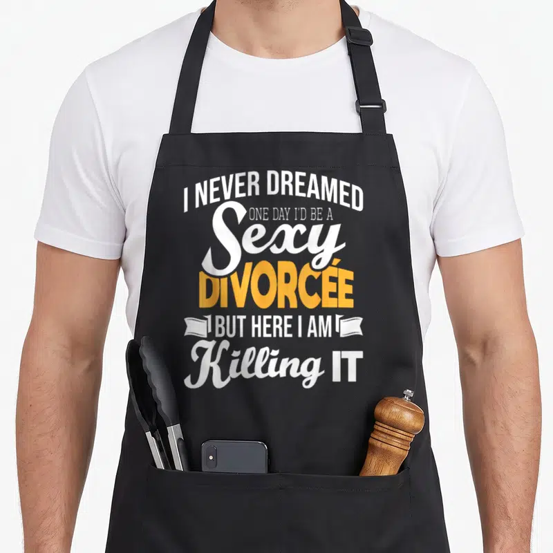 Dreamed divorce party apron - I Never Dreamed Sexy Divorcée text with ribbon ends in white and yellow — shown on a black cotton canvas apron against a white background