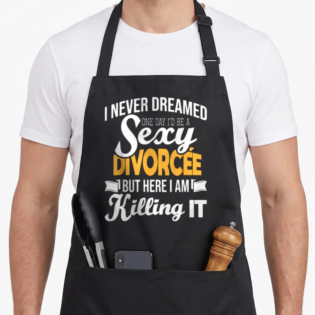 Dreamed divorce party apron - I Never Dreamed Sexy Divorcée text with ribbon ends in white and yellow — shown on a black cotton canvas apron against a white background