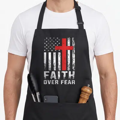 Faith american flag apron - Red cross over distressed white stripes with stacked FAITH OVER FEAR text — shown on a black cotton canvas apron against a white background