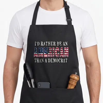 Would politician apron - Distressed white text reading I'd Rather Be An American Than A Democrat with flag pattern — shown on a black cotton canvas apron against a white background