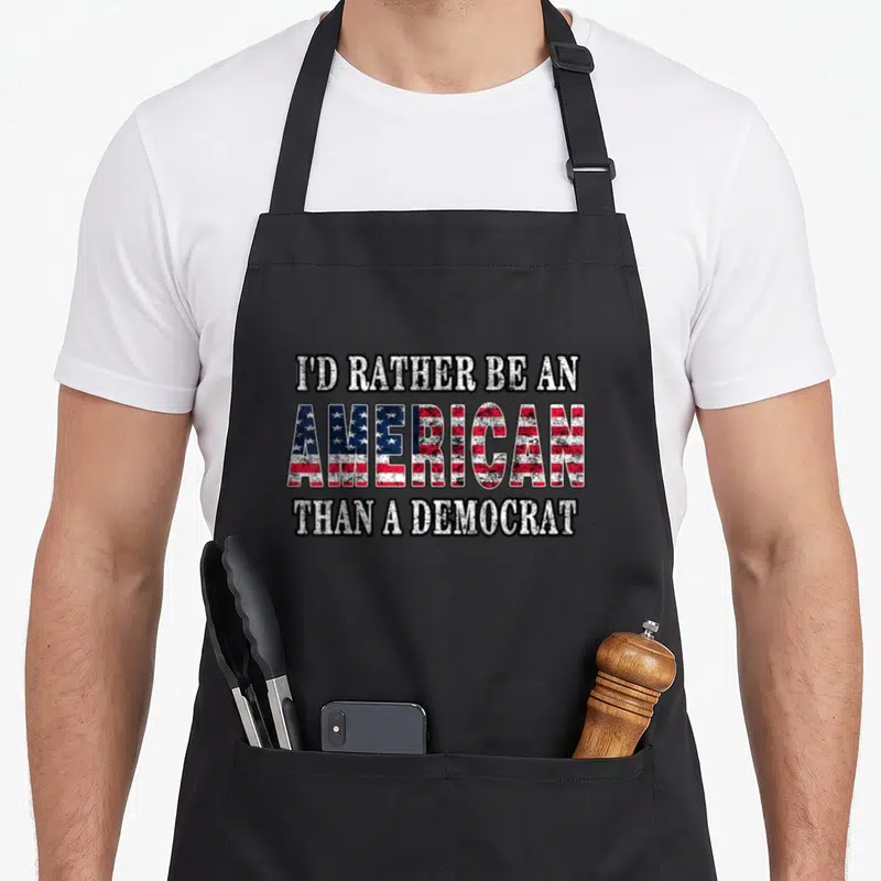Would politician apron - Distressed white text reading I'd Rather Be An American Than A Democrat with flag pattern — shown on a black cotton canvas apron against a white background