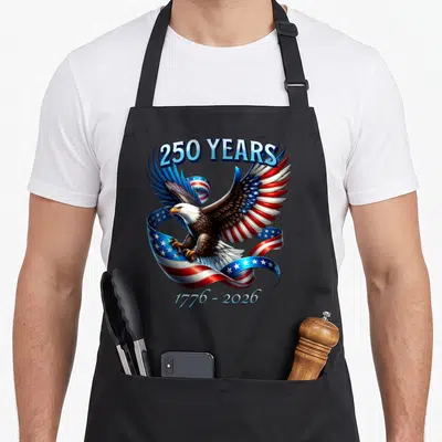 Eagle flag patriotic aprons - Bald eagle with winding red white and blue flag ribbon and 250 years 1776 2026 text — shown on a black cotton canvas apron against a white background