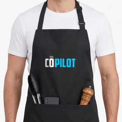 Aviation chef and co aprons - COPILOT text in white and blue with a diamond ring icon above the O — shown on a black cotton canvas apron against a white background