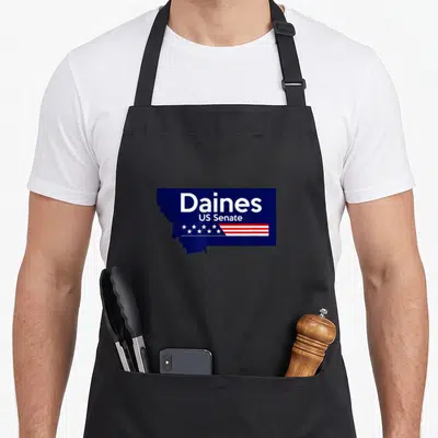 Steve senator apron - Daines US Senate text in blue Montana shape with stars and stripes — shown on a black cotton canvas apron against a white background