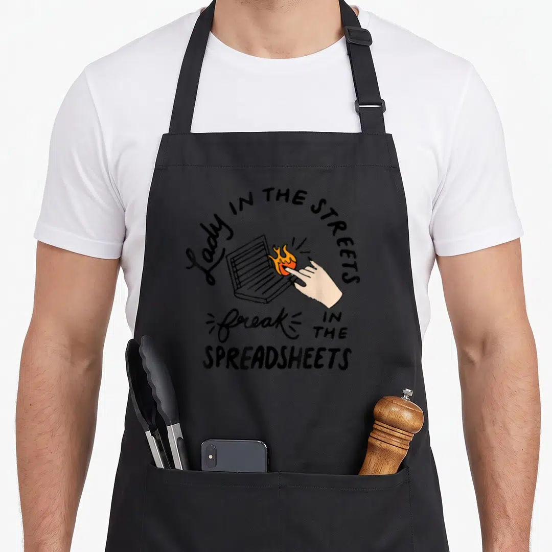 Street accountant apron - Hand pointing at burning laptop with Lady in Streets Freak in Spreadsheets text — shown on a black cotton canvas apron against a white background
