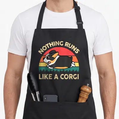 Funny run corgi apron - Tricolor corgi running over teal forest with red orange yellow striped sun — shown on a black cotton canvas apron against a white background