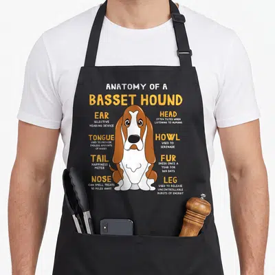 Hound anatomy dog apron - Cartoon Basset Hound with labels defining ear selective hearing and nose smell range — shown on a black cotton canvas apron against a white background