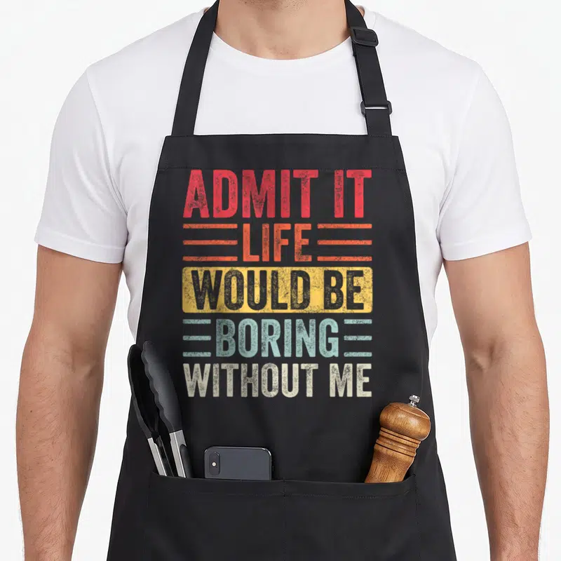 Admit novelty apron - Stacked text ADMIT IT LIFE WOULD BE BORING WITHOUT ME in red orange yellow blue beige distressed — shown on a black cotton canvas apron against a white background