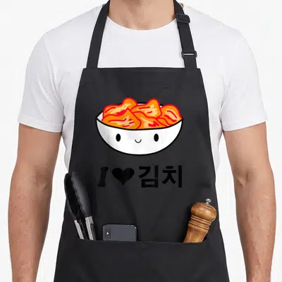Kimchi korean apron - Cartoon white bowl with orange kimchi and I love Korean text — shown on a black cotton canvas apron against a white background