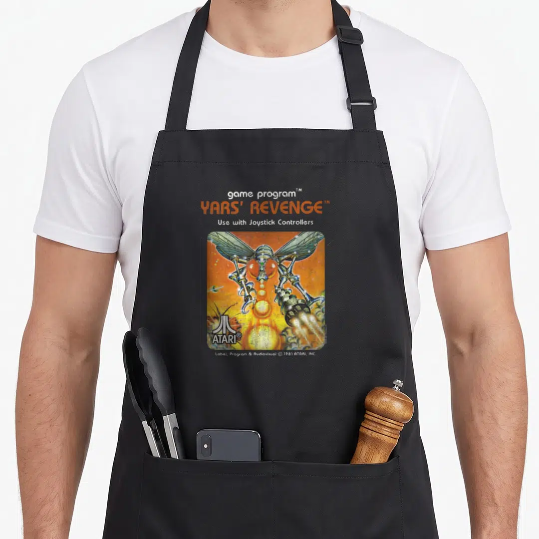 Yar video game apron - Yars' Revenge robotic insect hovering over planet with orange yellow silver white text — shown on a black cotton canvas apron against a white background