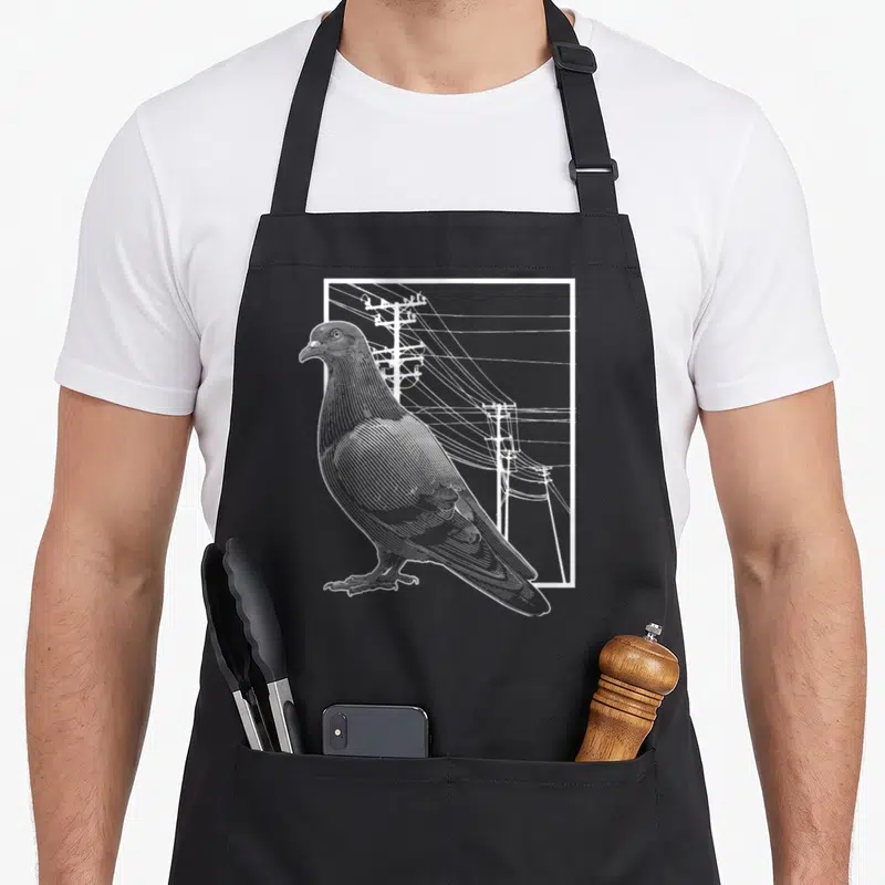 Pigeon breeder bird apron - White line-art pigeon standing in front of utility poles inside a rectangular border — shown on a black cotton canvas apron against a white background