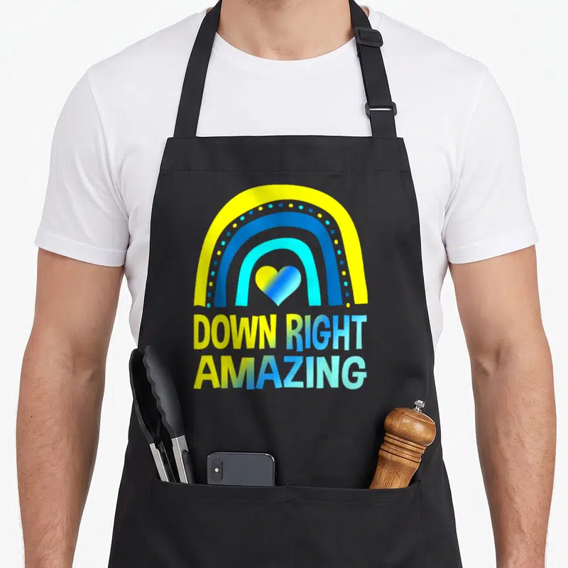 Right amazing aprons - Rainbow arch with heart and gradient text reading DOWN RIGHT AMAZING in yellow and blue — shown on a black cotton canvas apron against a white background