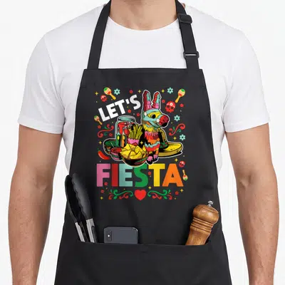 Fiesta mayo apron - Cartoon piñata with tacos and maracas surrounding LET'S FIESTA text — shown on a black cotton canvas apron against a white background