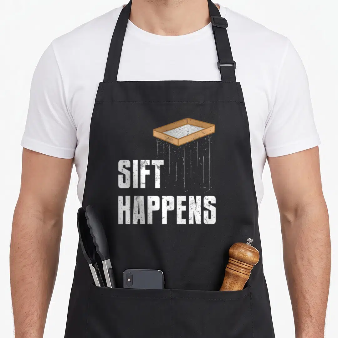 Sift archaeologist apron - Brown sifter above white distressed SIFT HAPPENS text — shown on a black cotton canvas apron against a white background
