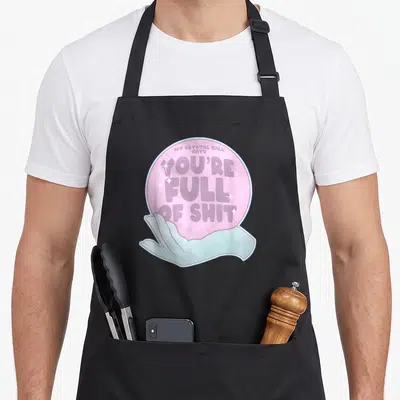 Ball goth apron - Pink crystal ball held by blue hand with sarcastic fortune text — shown on a black cotton canvas apron against a white background